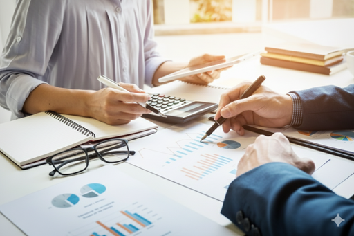 racunovodje-analiza-prihodi-rashodi-kalkulator-tablet-uredski-stol Računovođe analiziraju izvještaje s grafovima “Prihodi” i “Rashodi” uz kalkulator, bilježnicu, naočale i tablet na svijetlom uredskom stolu.